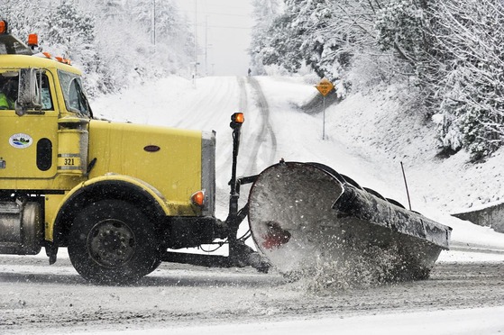 A yellow snow plow clearing a road in the snow