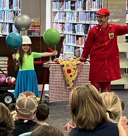 Child holds two sticks with spinning globes on them while wearing a hat with another stick and spinning globe while an adult cheers