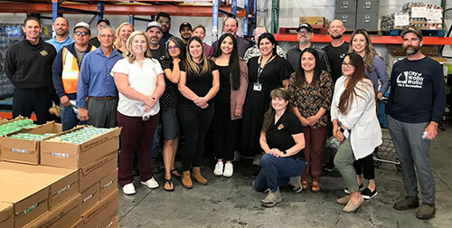 Twenty-four City staff members pose for a group photo in a food bank