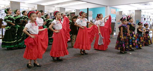 Children in traditional Mexican outfits perform group dances in the library