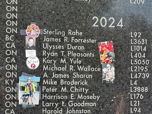 The names of fallen firefighters engraved in granite, with some photos and stickers taped to it