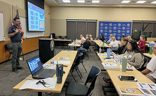 A standing City employee gives a presentation to a group of people seated at tables