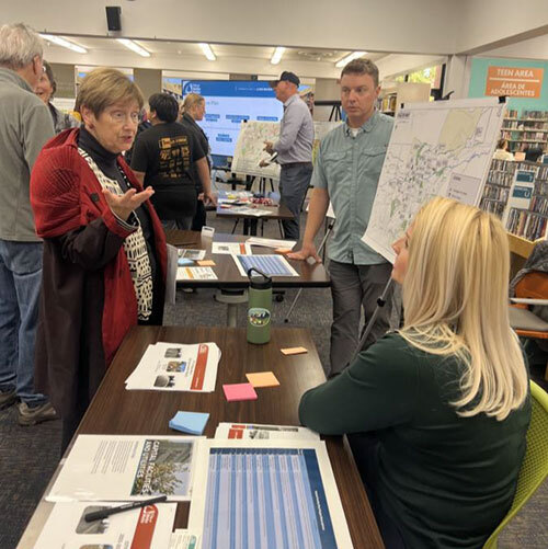 Three City staff members speak with people at an open house in the library