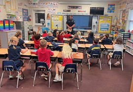 A firefighter stands in front a classroom of grade-school students while teaching about fire safety