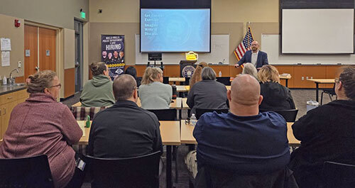 People sit at tables in front of a screen while a person presents information