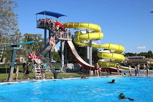People swim, jump into, and gather around the large pool at Veterans Memorial Pool