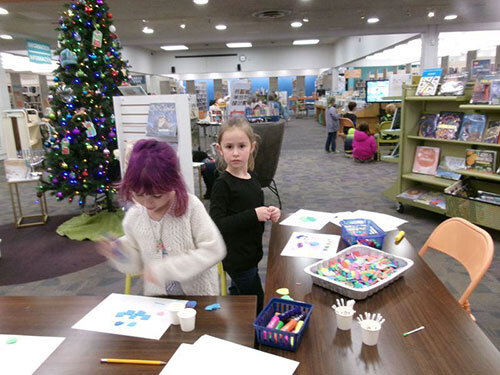 Two children make paper crafts on tables in a library