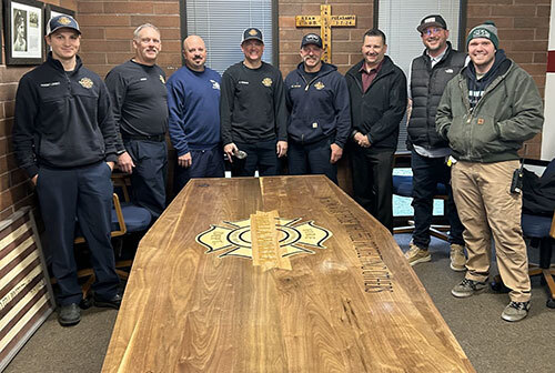 Eight fire and penitentiary staff members stand next to a glossy wooden table with a logo in the center