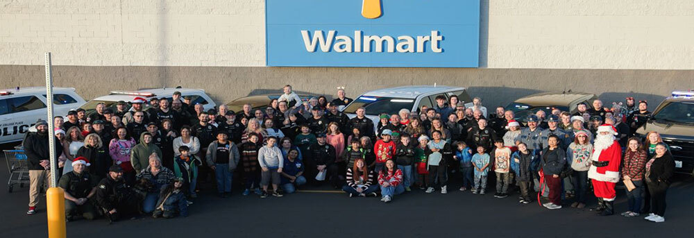 A group of dozens of children and law-enforcement personnel poses for a photo in front of a Walmart store