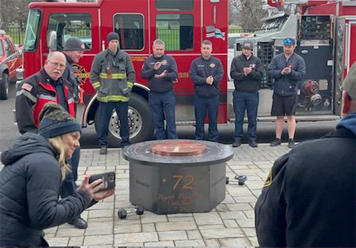 Firefighters and family members gather around a gas fire pit with Ryan Pleasants' #72 on its side