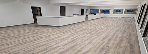 Large room under construction, with windows, a long counter, vinyl wood flooring and blank white walls
