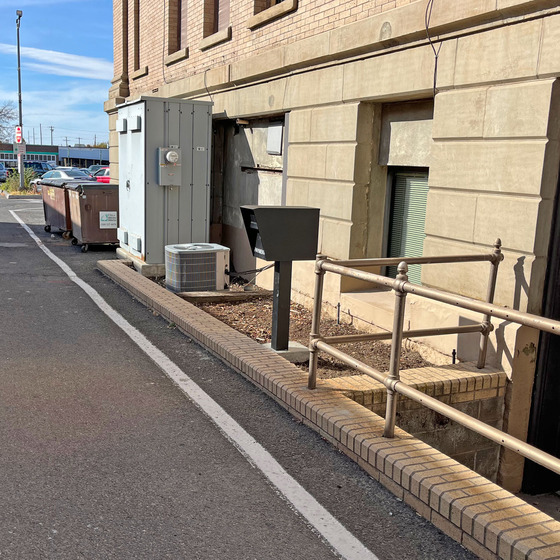 A black payment drop box mounted on a post in the alley next to Walla Walla City Hall