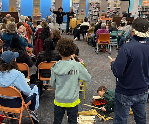 Library patrons use percussion instruments while musicians guide them