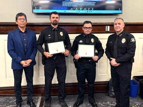 A mayor and three police personnel — two holding awards — stand in the Council Chambers