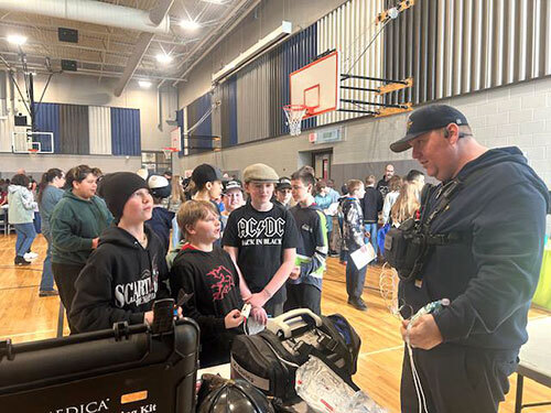 A CARES member shows medical equipment to three students in a gymnasium