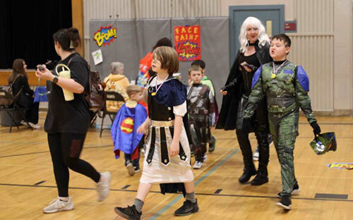 Mothers and children dressed in superhero costumes participate in events in a gymnasium