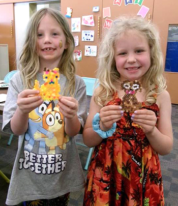Two young children hold animal crafts they made at the library