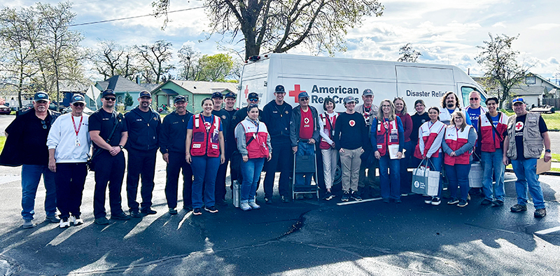 24 people — fire personnel and Red Cross volunteers — stand for a group photo in front of a Red Cross van