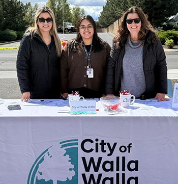 Three Human Resources staff members stand behind a table with employment information during an outdoor job fair