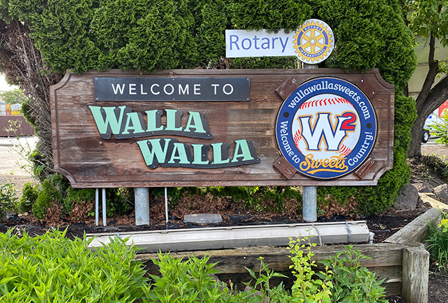 Welcome to Walla Walla sign with vegetation above and below it and a smaller, round sign promoting the Walla Walla Sweets baseball team