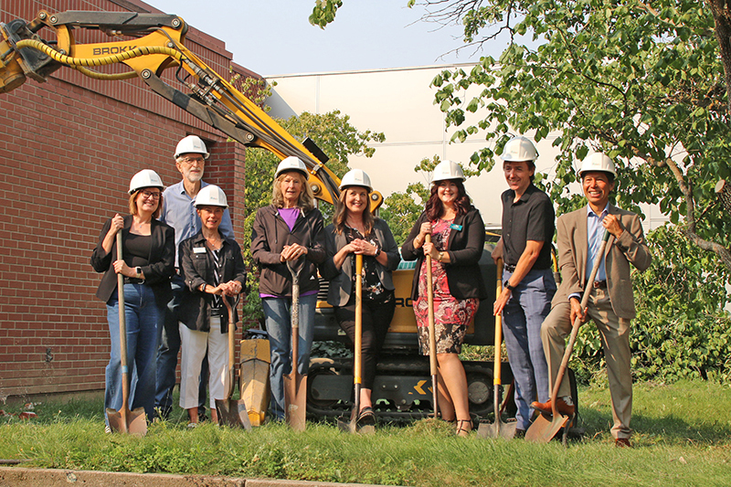 Eight people wearing hard hats and holding shovels stand outside the Walla Walla Public Library during a groundbreaking ceremony