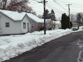 During winter, a plowed residential street in Walla Walla with the plowed snow pushed into a berm around 18 inches tall along the side of the street