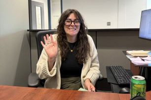Person sitting in a cubicle waves to the camera
