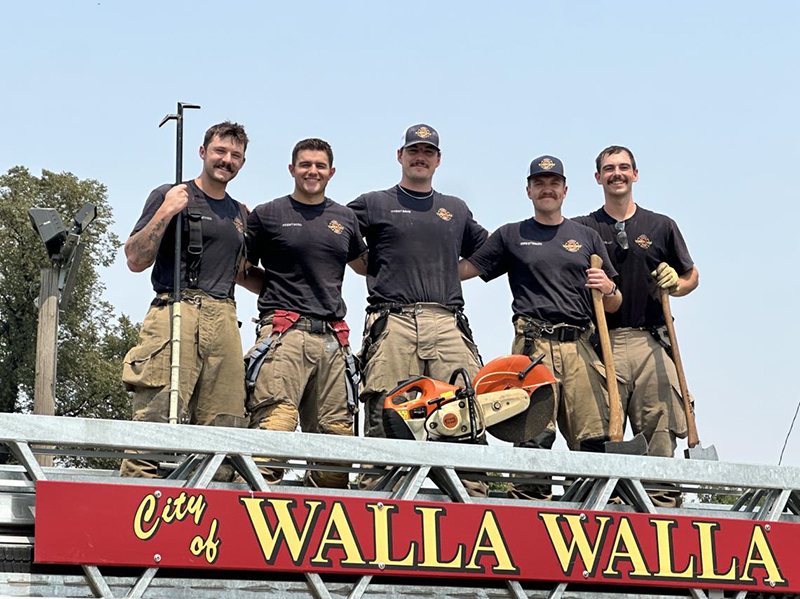 Five firefighters hold tools and stand on top of a Walla Walla Fire Department fire engine