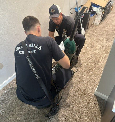 Two fire personnel work on an upright vacuum in a carpeted hallway