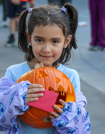 A child holds a pumpkin carved into a jack-o'-lantern and a red envelope