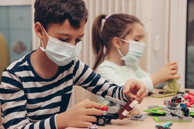 A boy and a girl wear face masks while playing with Legos. 