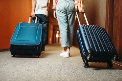 Two youth walking down a hotel hallways with suitcases. 