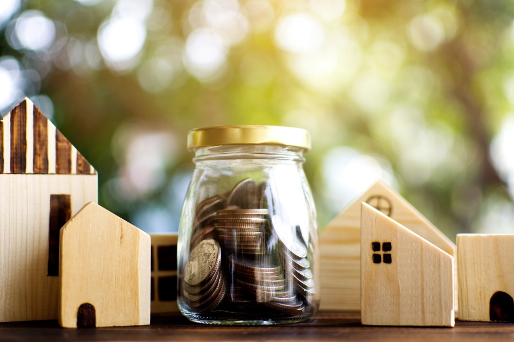 Small wooden houses surrounding a jar filled with coins. 