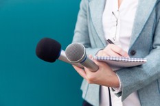 reporter with note pad taking notes, holding microphone