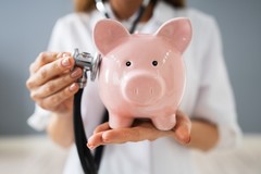 Person holding a piggy bank listening to "heartbeat" with a stethescope 