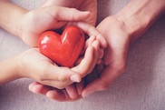 Two pair of hands holding a carved and painted red heart