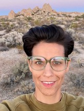  Photo of Tatsuko Go Hollo, DCYF ESIT Technical Assistance Manager, standing in front of a beautiful desert landscape, with a purple sunset sky.