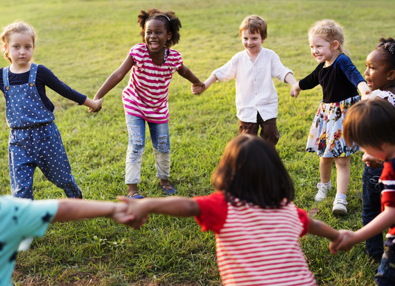 Kids hold hands in a circle as they play in a park. 