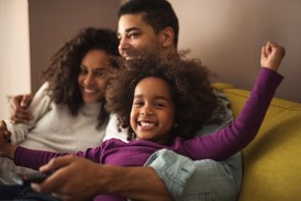 Little girl smiles gleefully while sitting with parents on couch. 