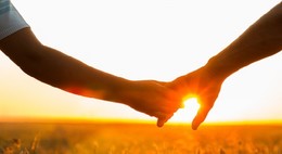 A parent and child hold hands with a sunset background.