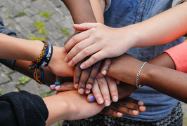 A group of youth put their hands together as a symbol of teamwork.