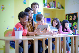 Children gather around teacher in preschool classroom. 