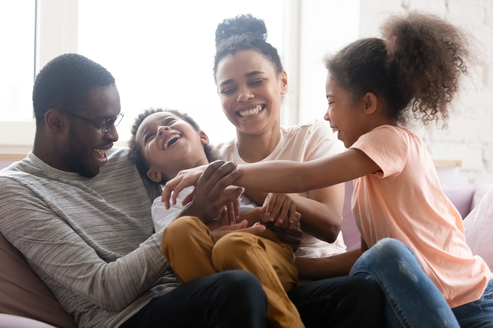 Family laughing together while big sister tickles little brother. 