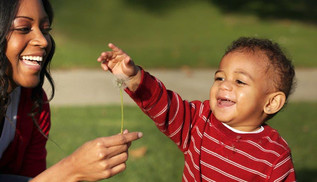 A mother holding up a dandelion for her toddler. 