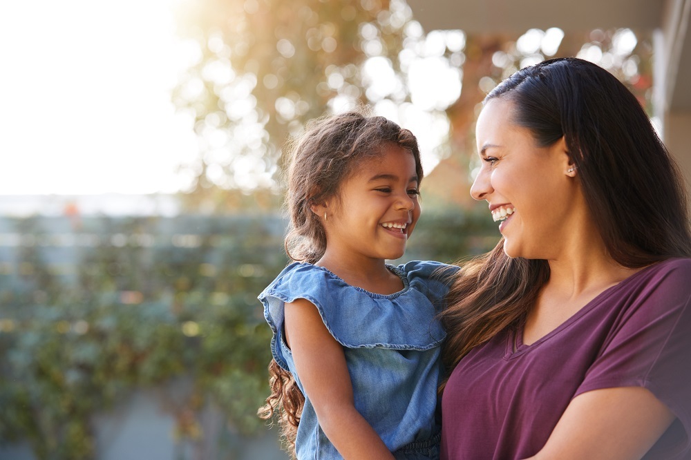 Mother holding her daughter and smiling at each other. 