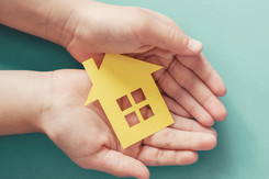 Pair of hands hold a paper house. 