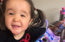 Photo of 3-year-old Opal, smiling and finger painting.