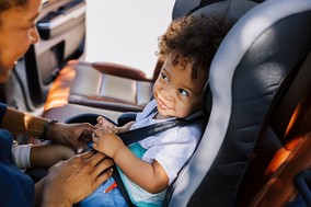 mother smiling at child in car seat, child smiling back