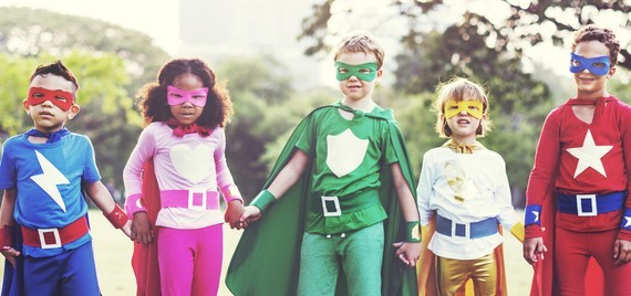 Children holding hands while wearing superhero costumes. 