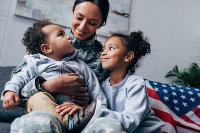 A mother in military uniform sits with her two young children. 